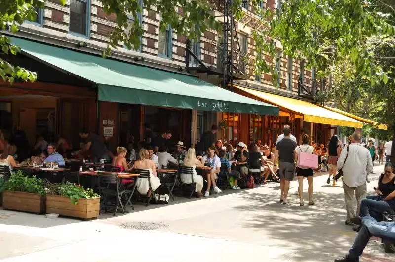 Diners at sidewalk tables under the green Bar Pitti awning on a sunny afternoon