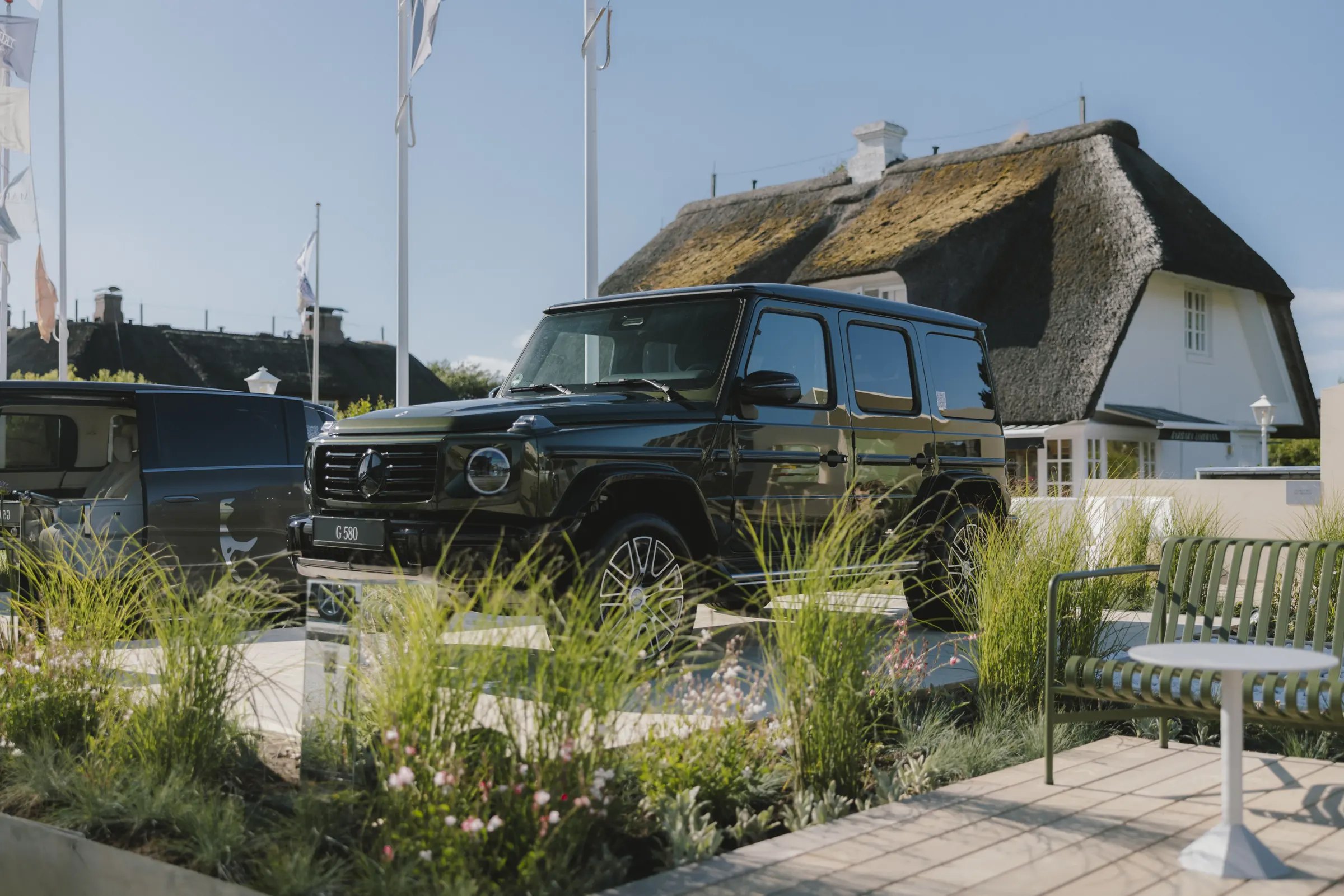 A black Mercedes-Benz G 580 parked outside a thatched house